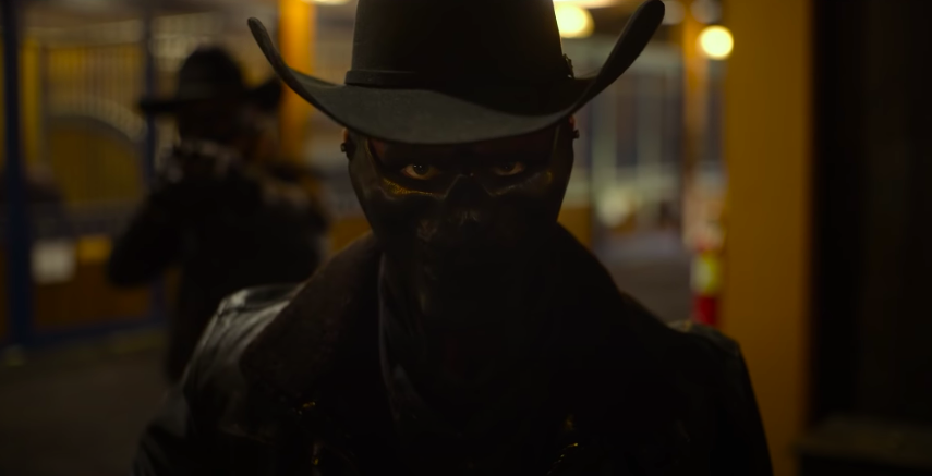 A man in a cowboy hat with his eyes darkened using makeup and a black mask covering only his nose and mouth