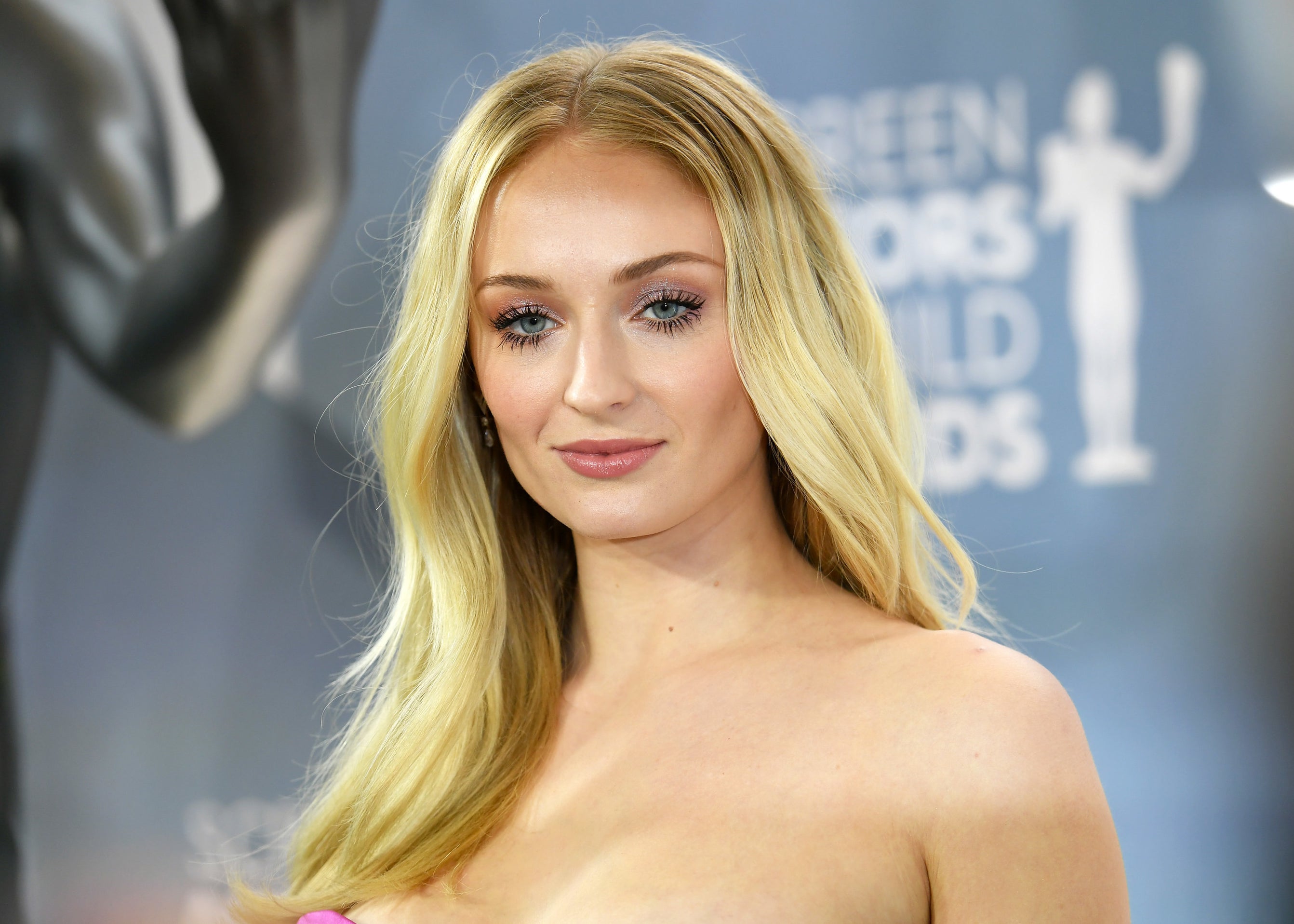 Sophie looks right into the camera in a strapless pink dress at an event