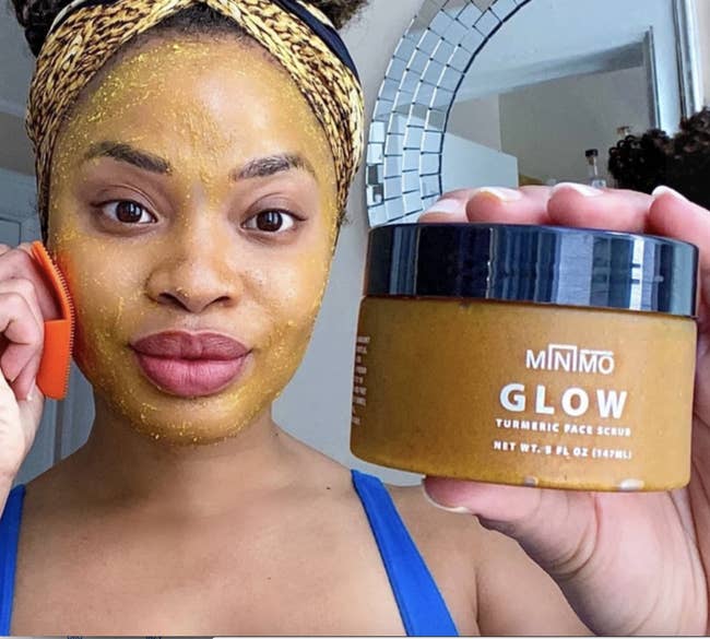 Model with turmeric face scrub on their face, holding the jar of it to the camera 