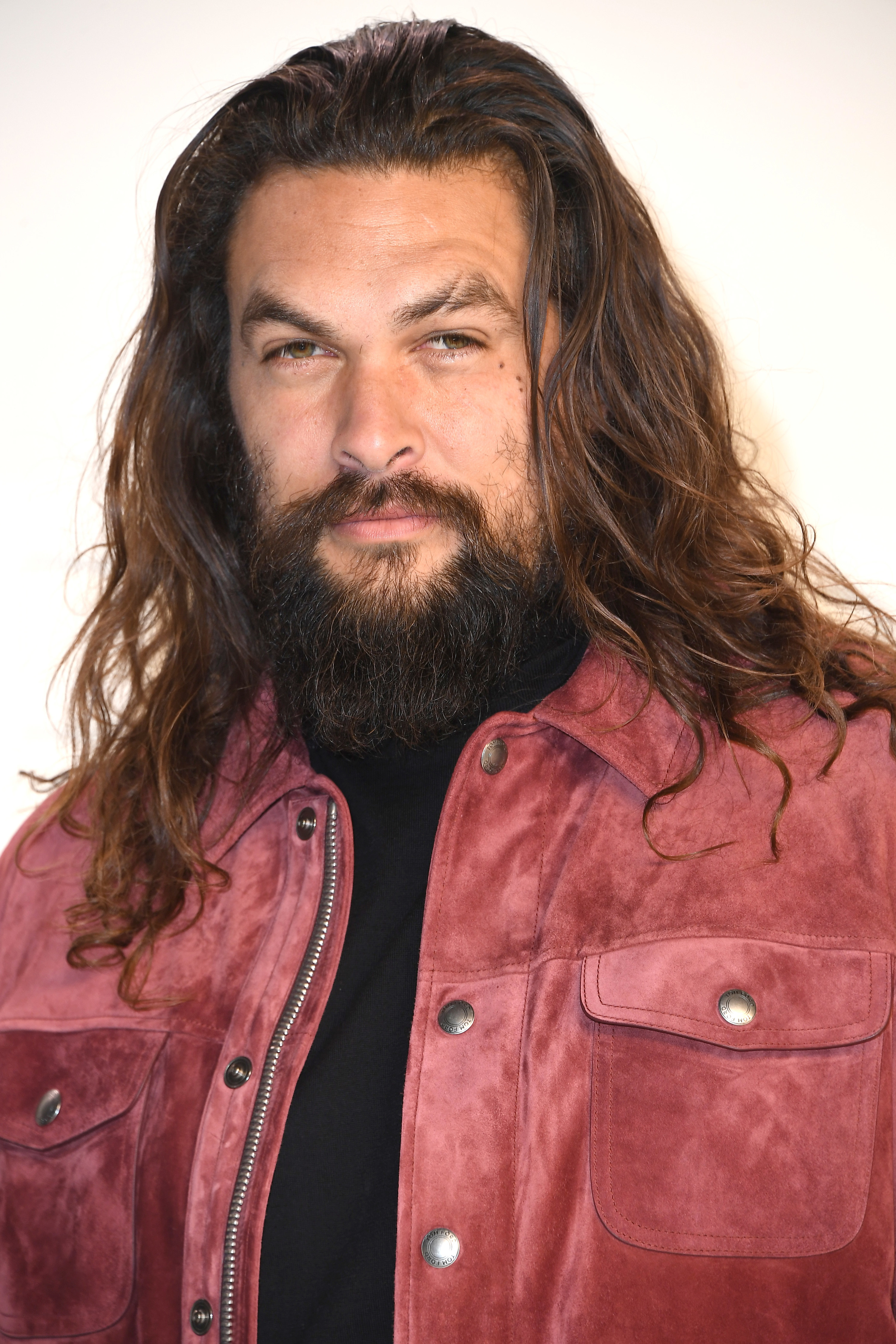 Jason Momoa smiles in a red suede jacket