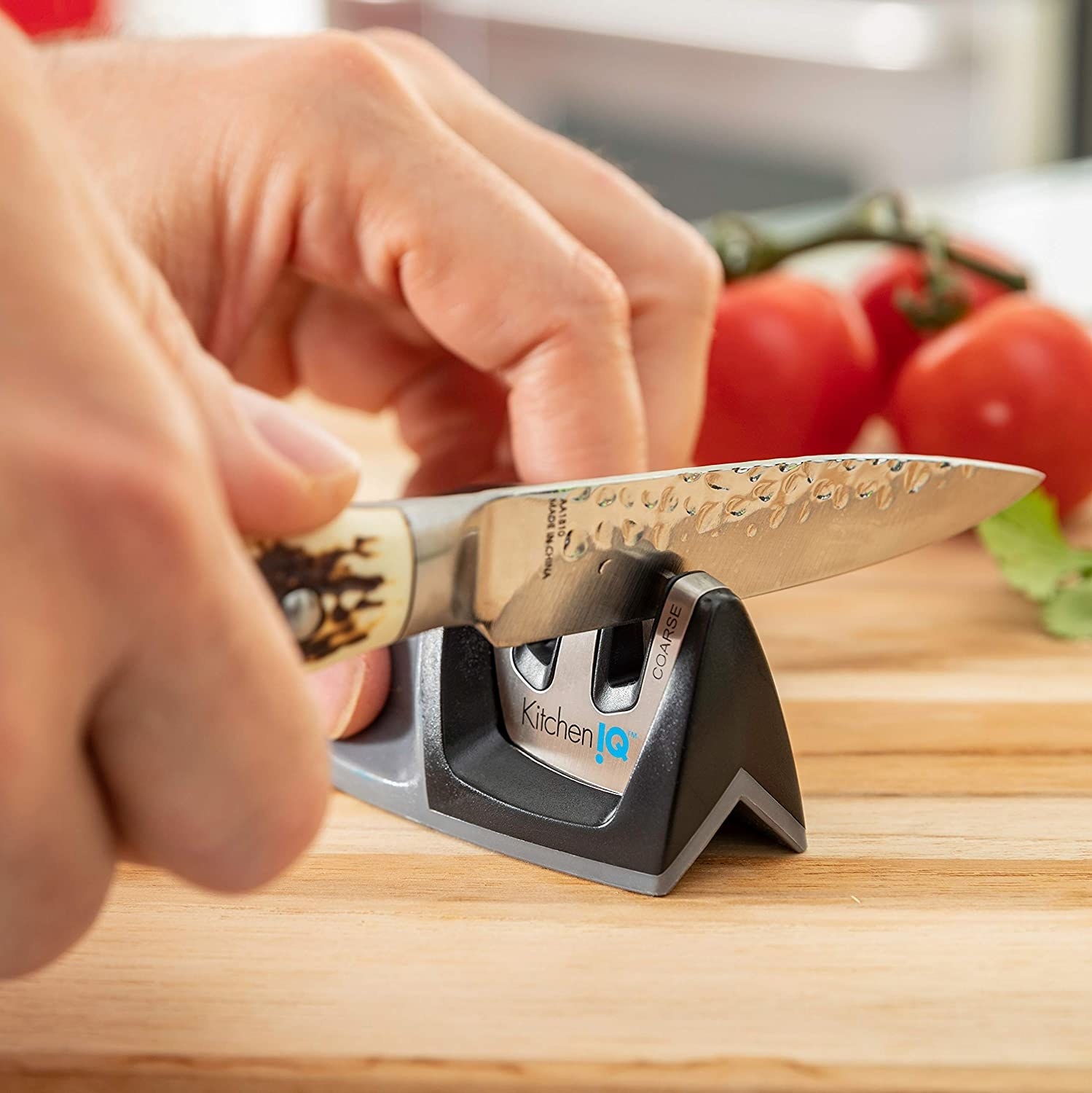 model sharpening knife in sharpener, tomatoes in background