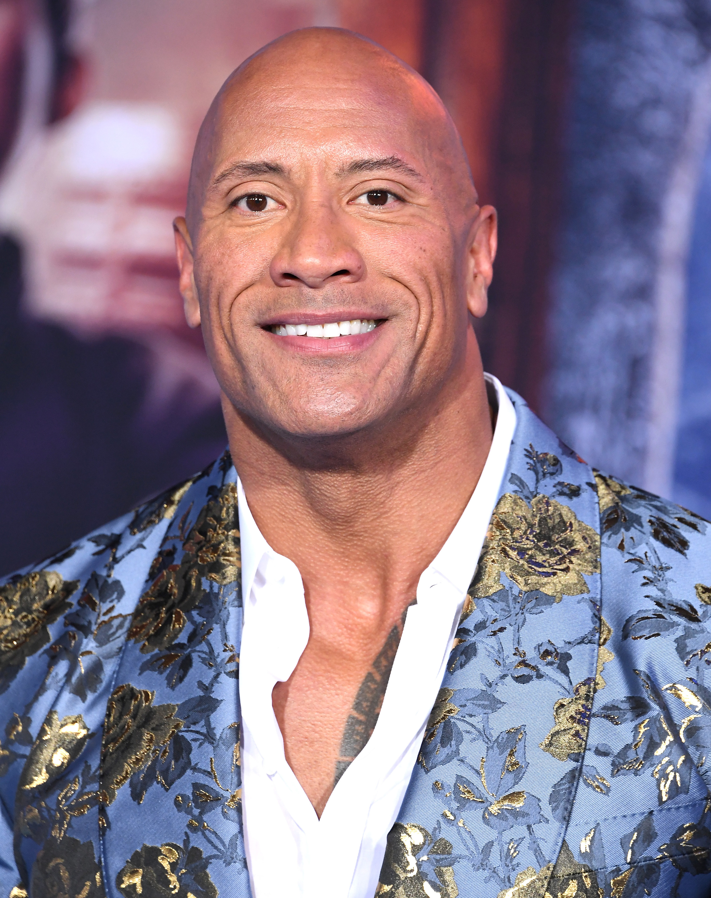 The Rock smiling as he wears a blue suit jacket with gold roses on it