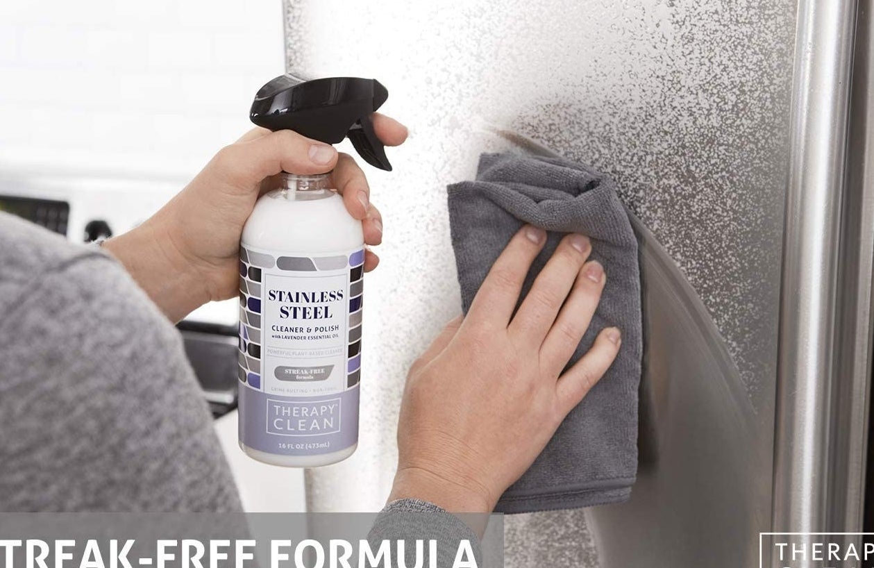 hand wiping fridge, sprayed with white cleaner, using a microfiber cloth