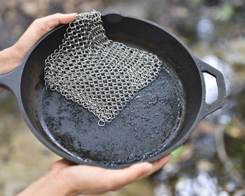 Model holding cast iron pan with chainmail scrubber