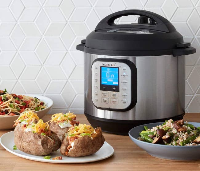 Instant pot surrounded by a pasta dish, baked potatoes, and a green beans and rice dish