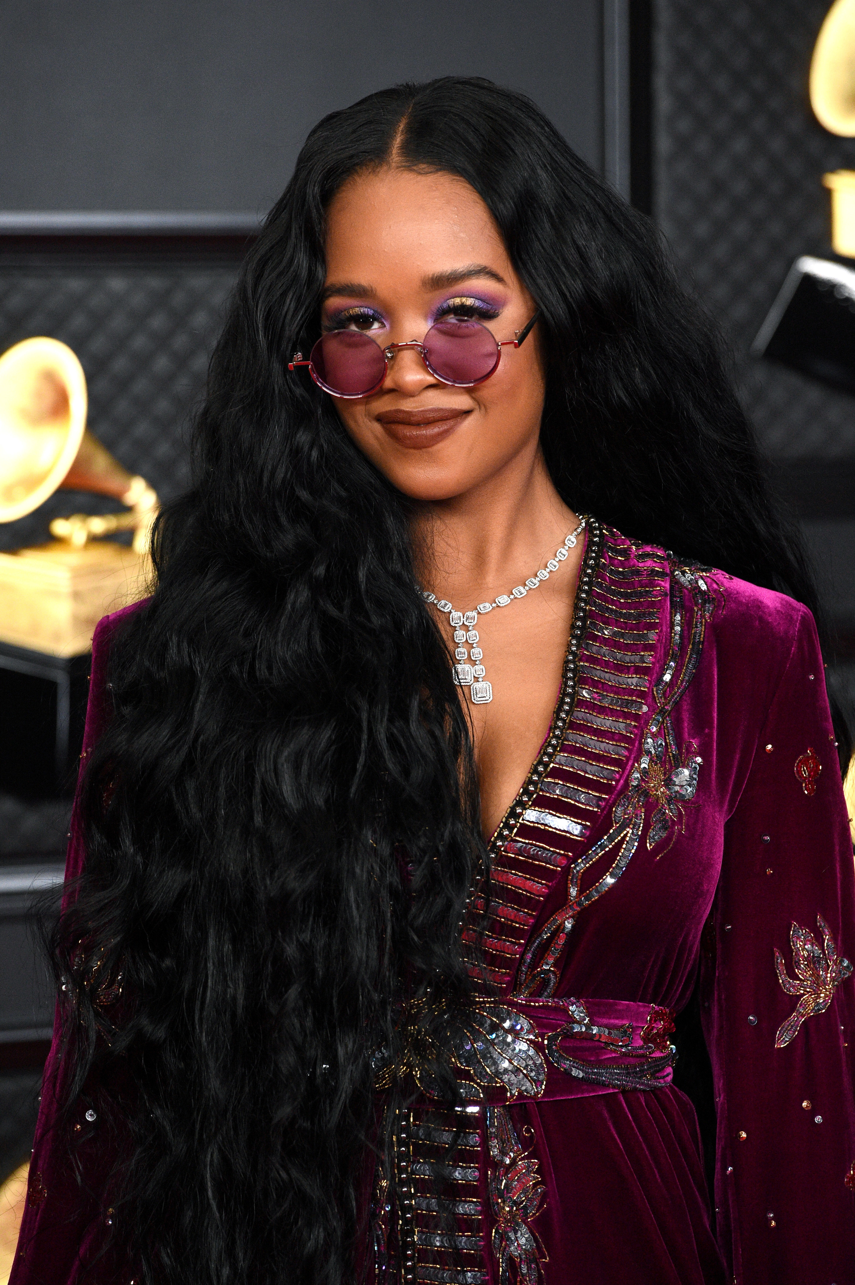 H.E.R. in a burgundy velvet dress with matching eyeshadow, wearing her hair in long loose waves