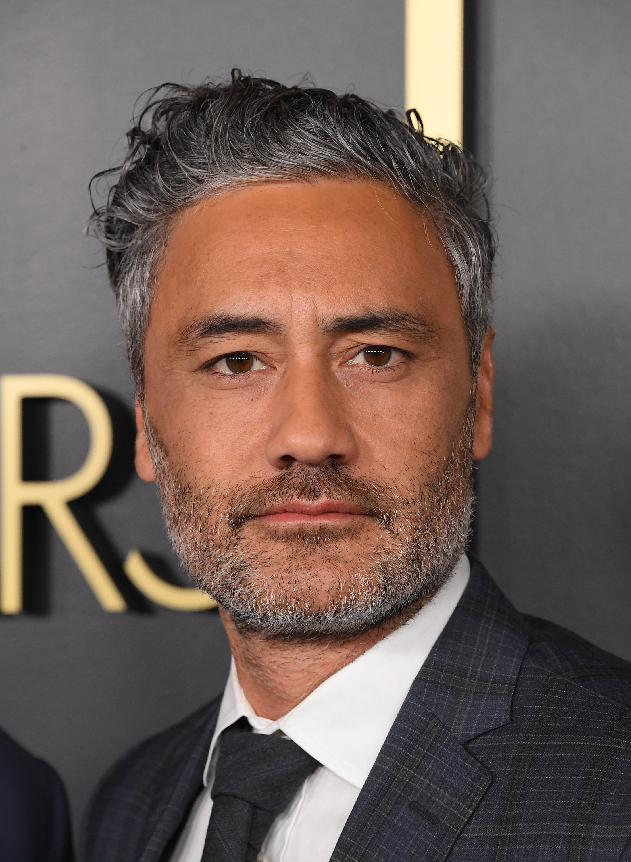 Taika Waititi looks directly at the camera in a suit at an award show