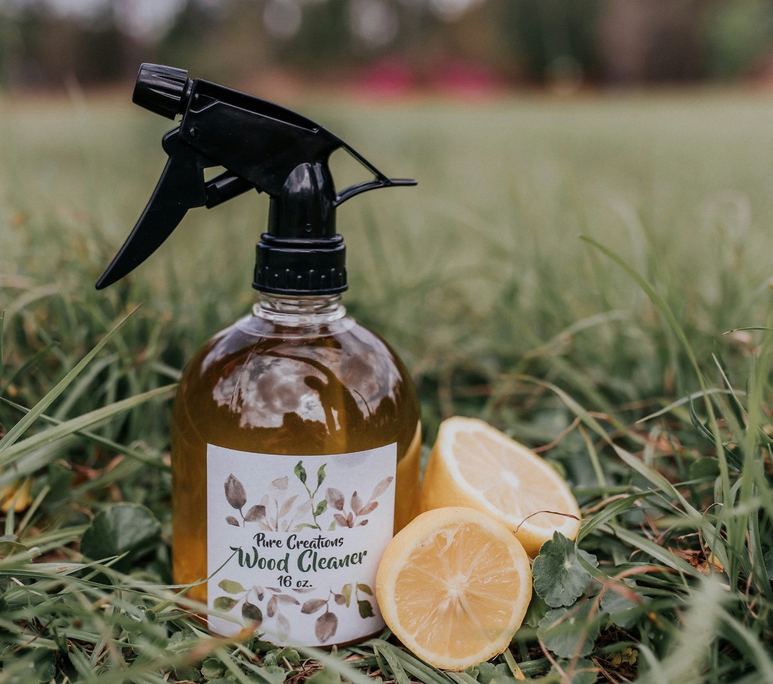 Bottle of Pure Creations Wood Cleaner placed in grass next to slice lemons