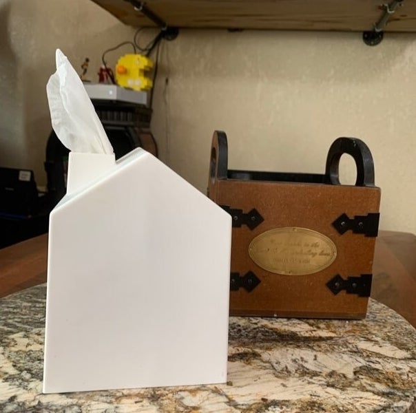 The tissue box, which is shaped like a house with a peaked roof, and the tissues poke out through the chimney