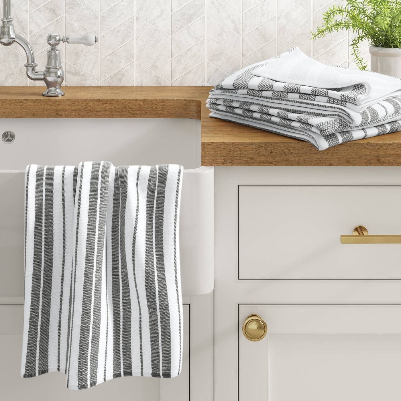 white and grey kitchen towel hanging on the side of a sink and stacked on the counter