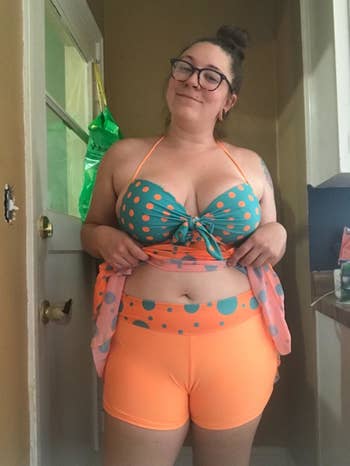 Reviewer wearing the orange and teal dotted swimsuit, holding up the flowy top to reveal short-style bottoms