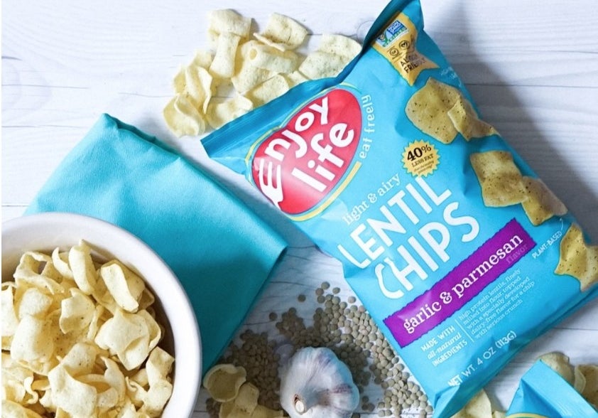 A bag of Enjoy Life&#x27;s garlic &amp;amp; parmesan lentil chips on a table next to a bowl of the product