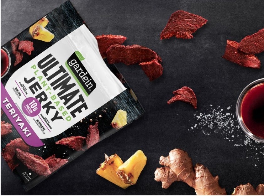 A bag of Gardein plant-based teriyaki jerky on a table with pieces of jerky on the table for display