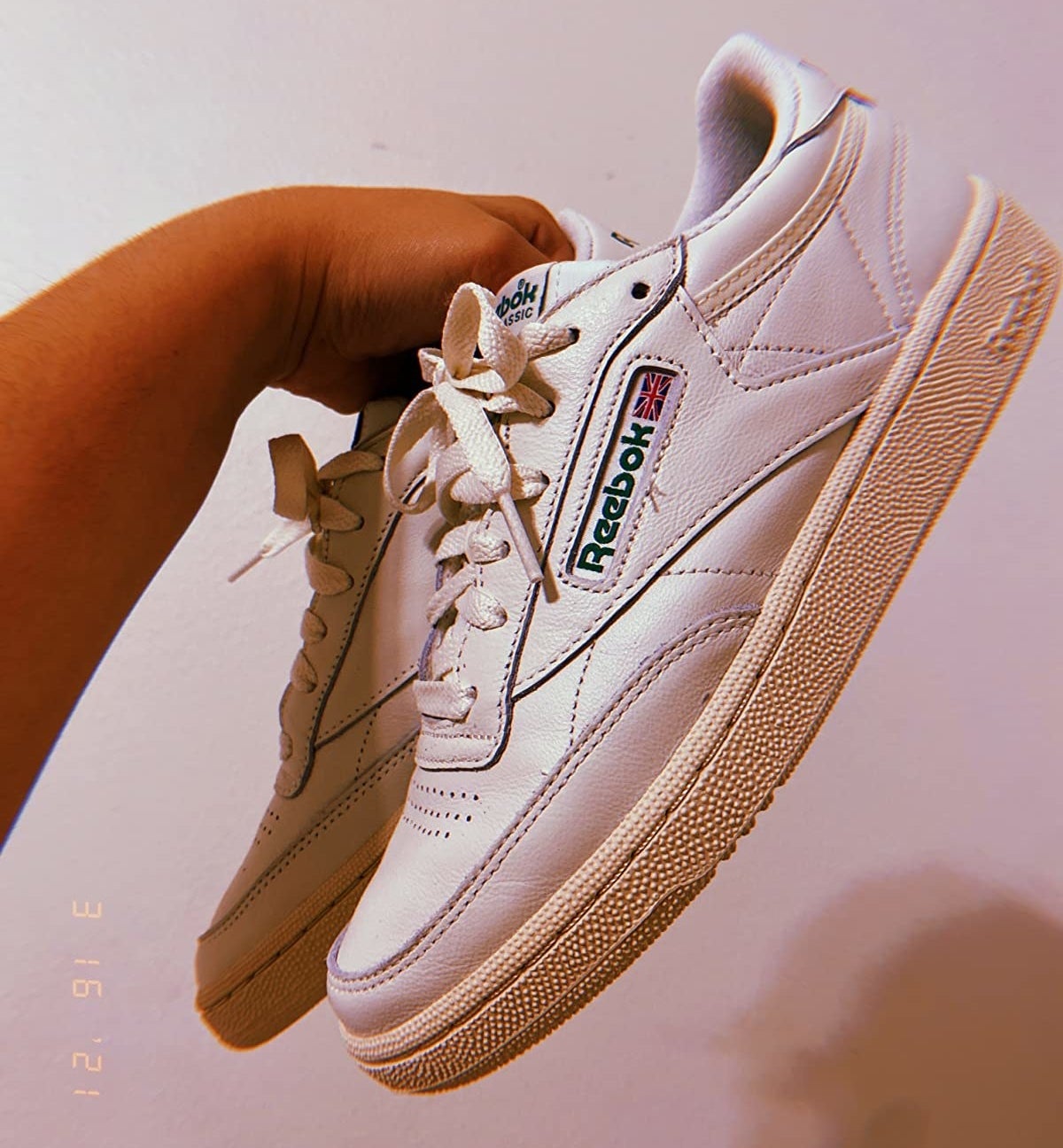 a reviewer holding up the off white sneakers with a green reebok label