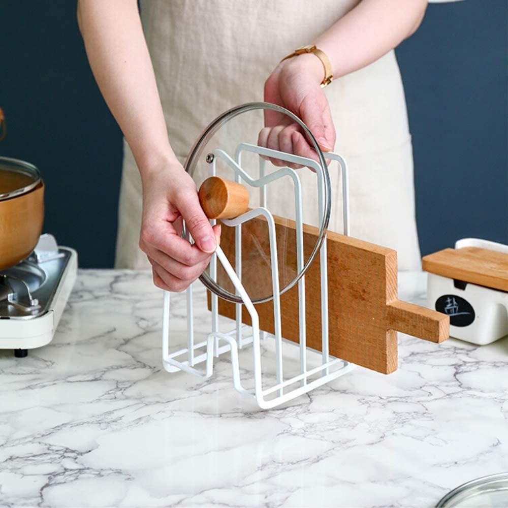 A person placing a pot lid in the cutting board rack