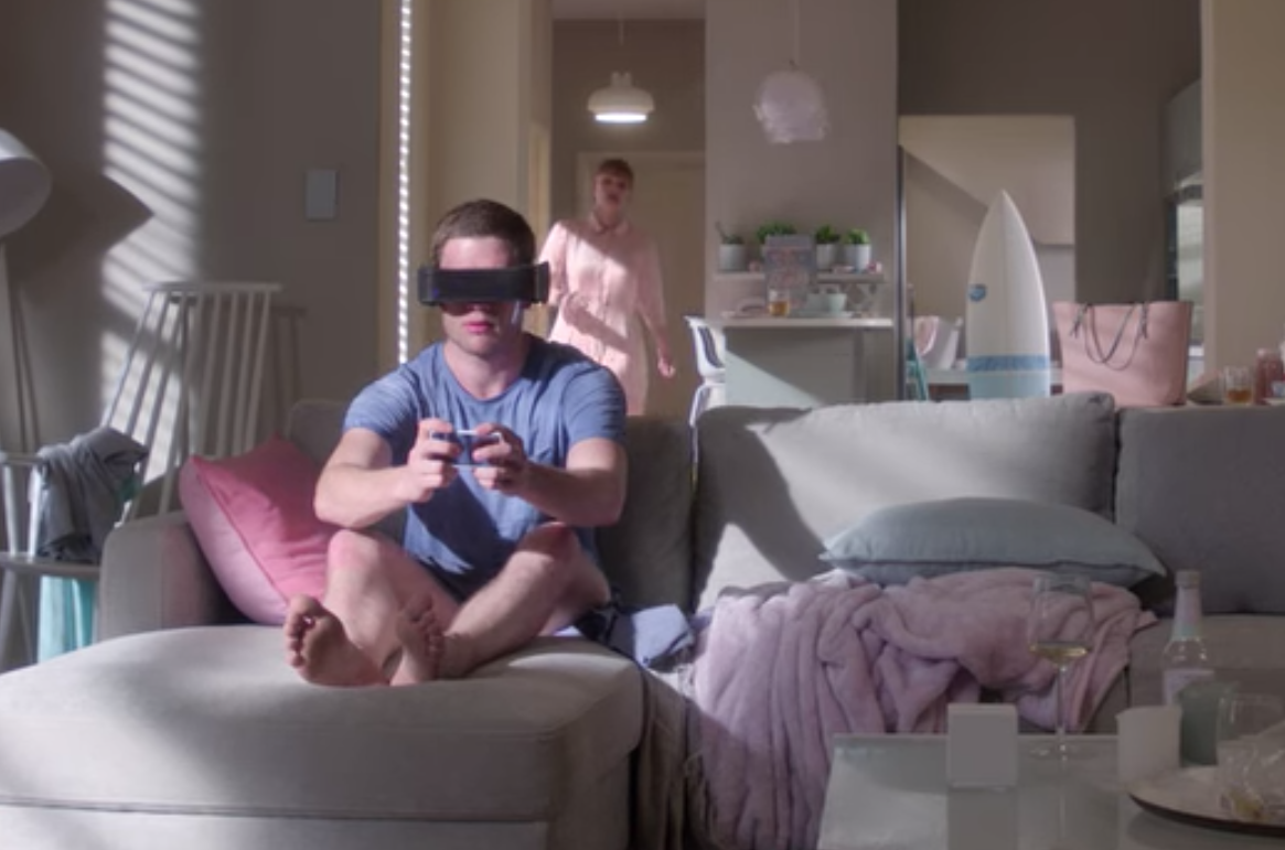 Lacie at home with her brother Ryan, who plays a video game on the couch, wearing a VR headset