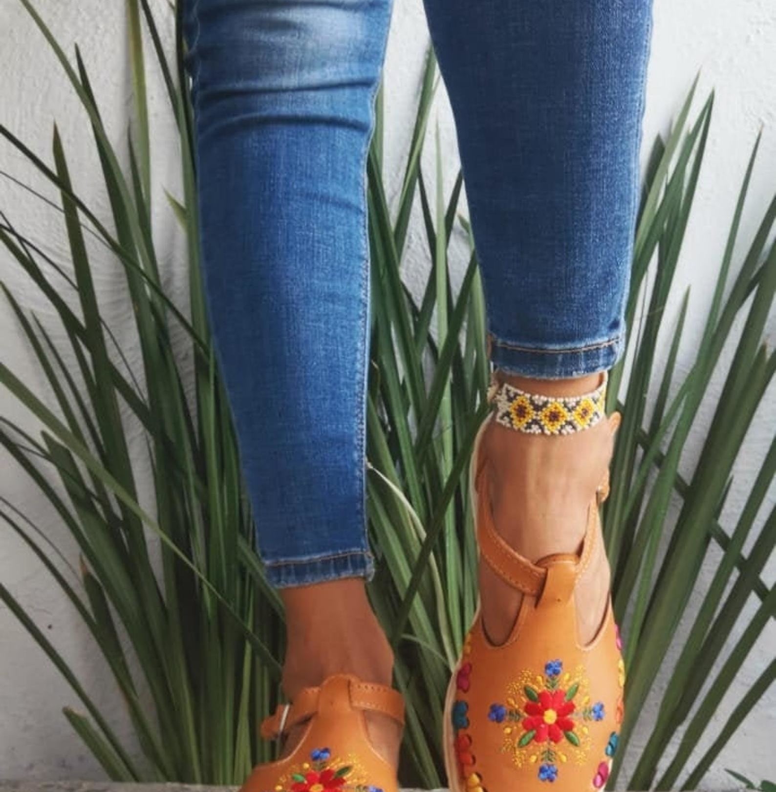 model wearing the tan shoes with shite sole and colorful flower on the top as well as colorful weaving between the sole and the top