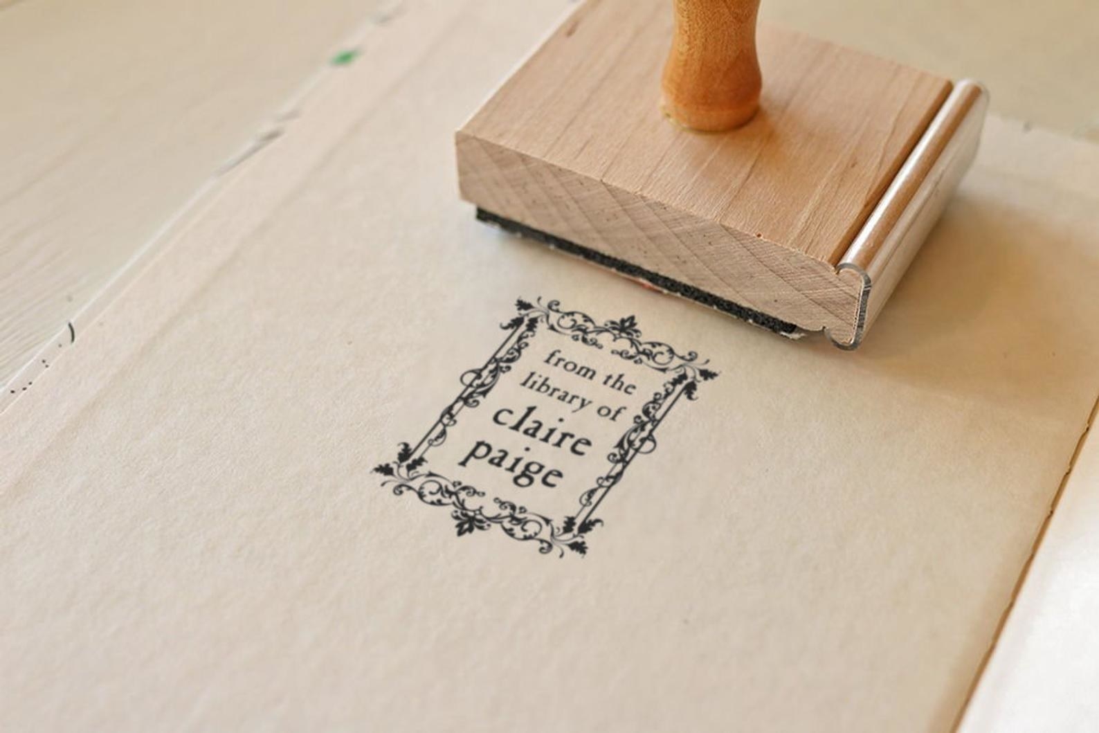 a light brown wood stamp with a rectangle floral stamp on a book page with the words &quot;from the library of claire paige&quot; on it