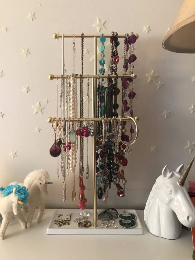Reviewer's gold three-tier jewelry stand with colorful necklaces on the handles and earrings on the bottom
