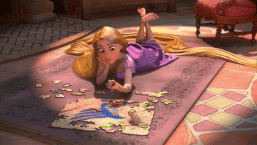 a gif of rapunzel doing a puzzle on the floor