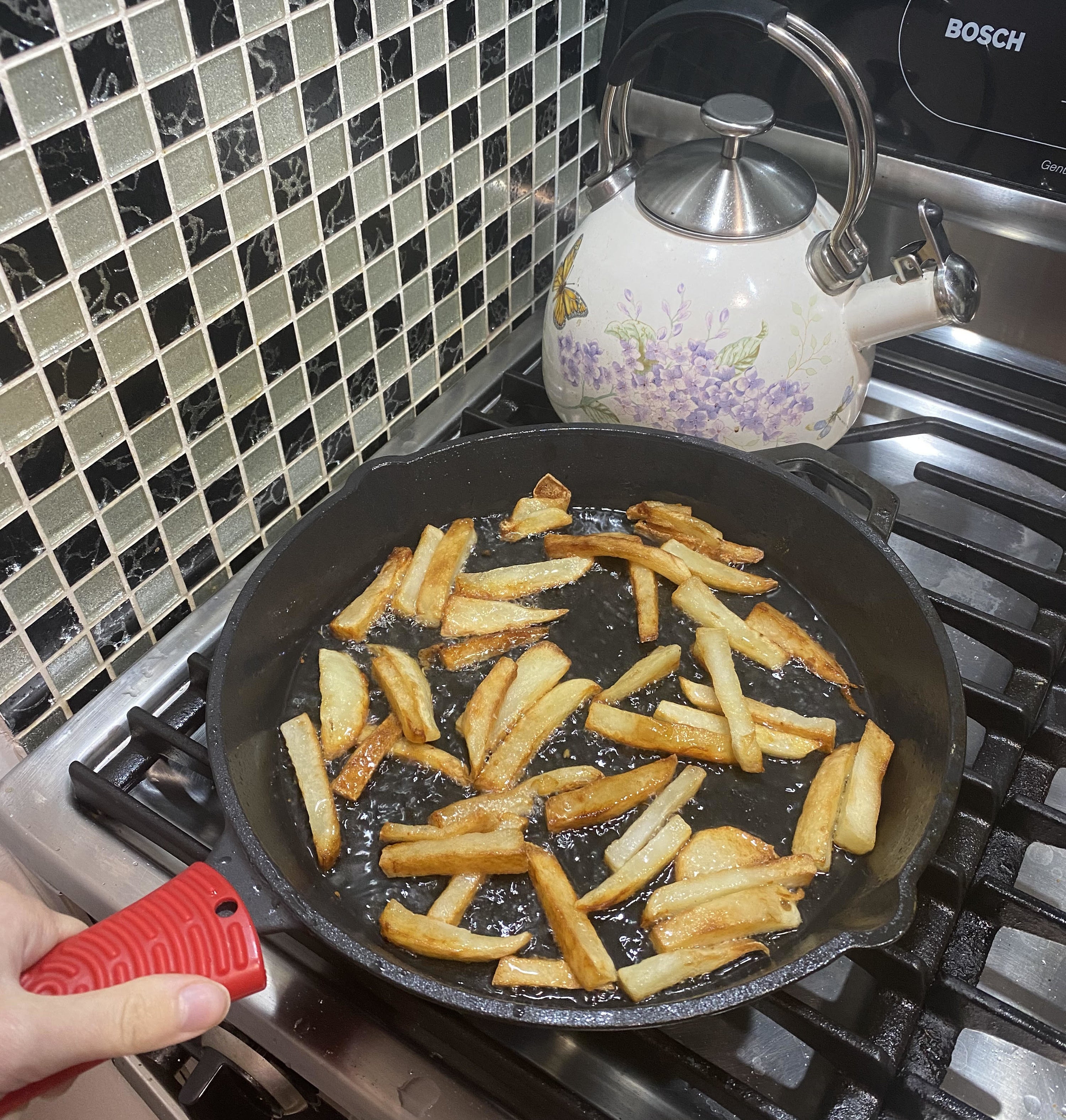 BuzzFeed writer using the red handle holder on a cast-iron pan with french fries in it 