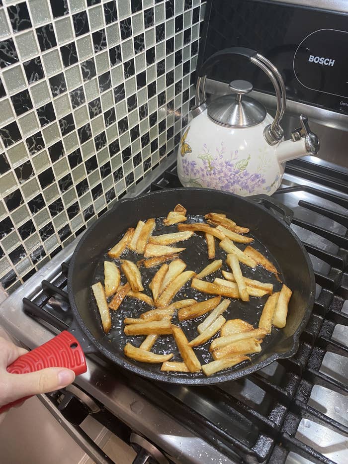the author using the red handle holder on a cast-iron pan with french fries in it 