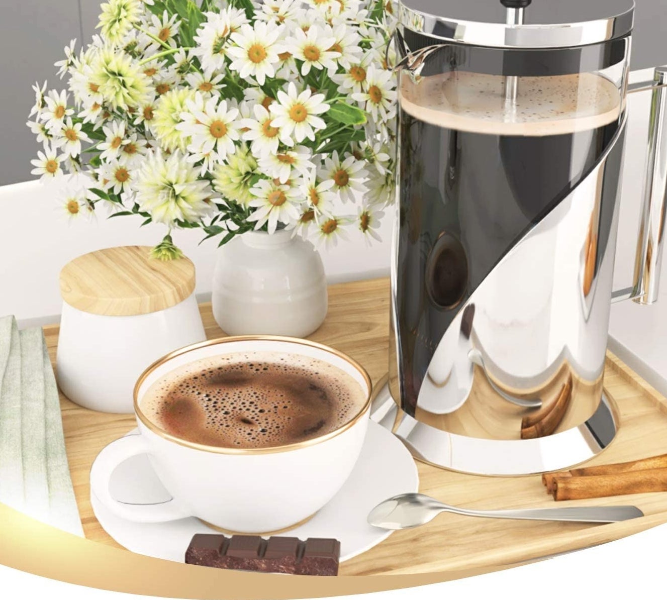 The stainless steel french press on a tray with a cup of coffee and a bouquet of daisies 