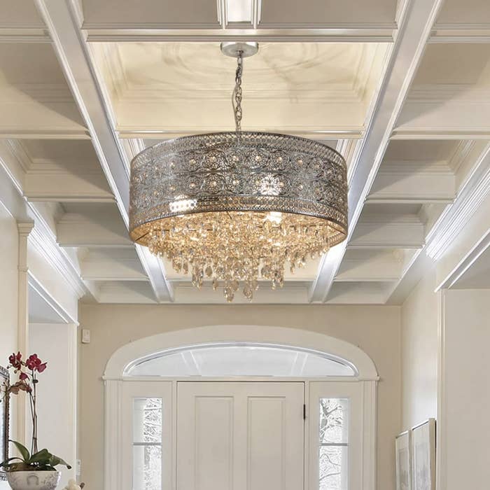 The chandelier has a brushed nickel cylindrical base and many small crystal drops coming down