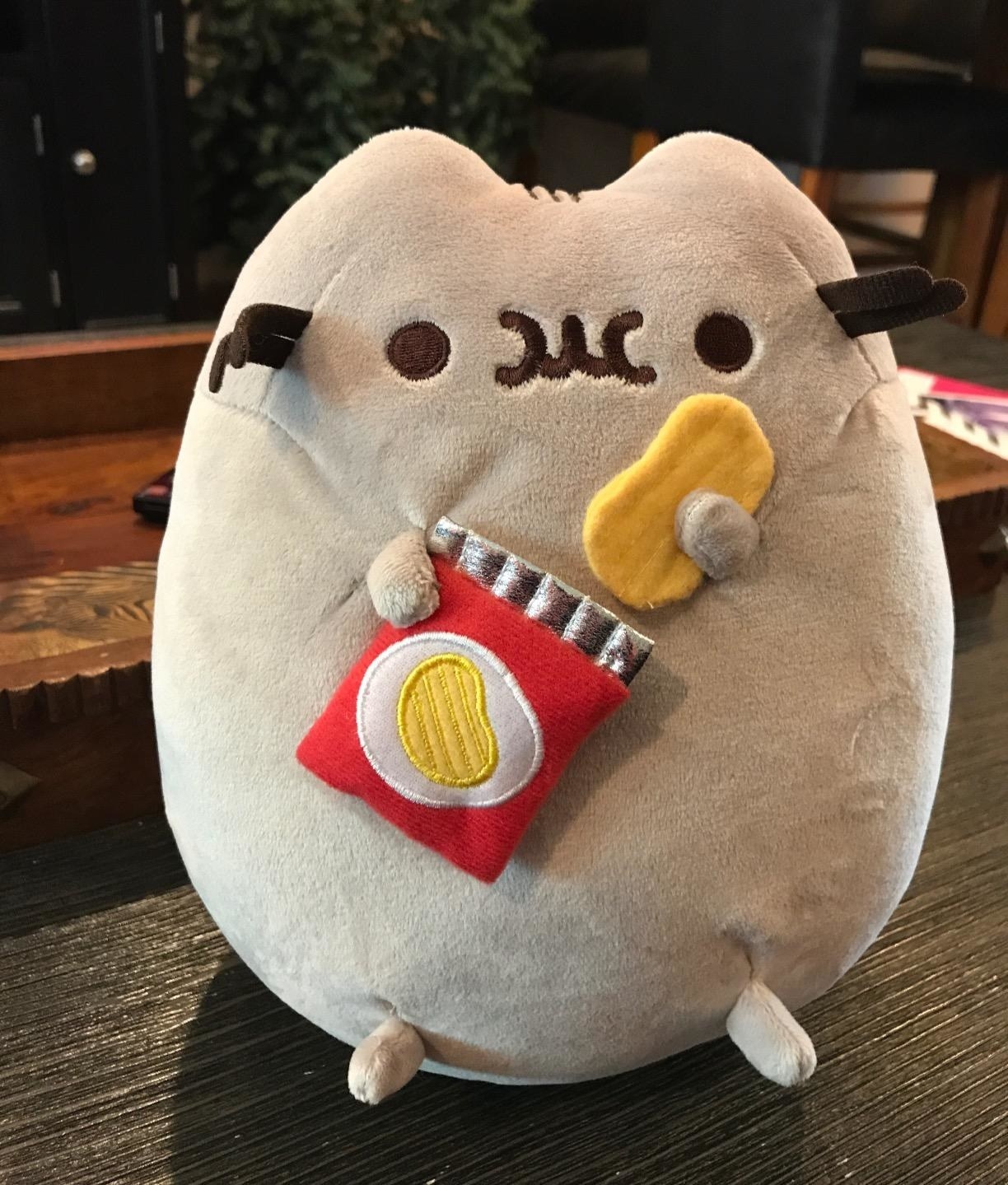 the plush holding a red bag of chips in one hand and a potato chip in the other, with a face like it&#x27;s chewing