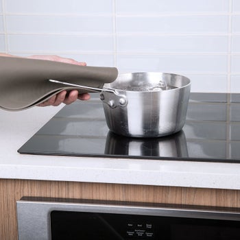 person using a beige multipurpose mat to grab a pot handle