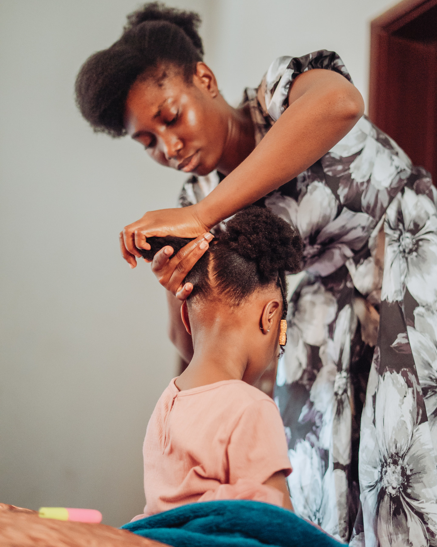 A woman leans over and ties a little girl's hair in a pigtail