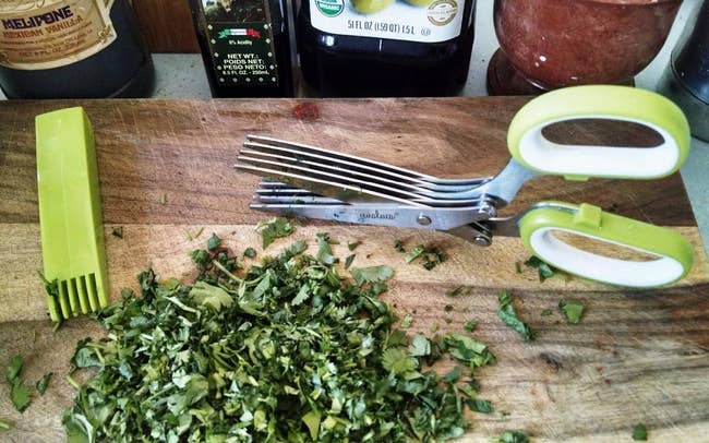 a reviewer photo of the multi-blade scissors next to a cleaning brush and a pile of chopped herbs 