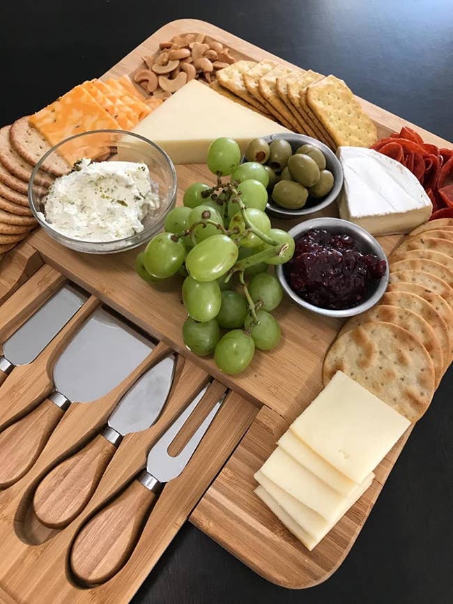 reviewer's wooden board with grooves for crackers and a knife drawer that slides out, filled with cheese, crackers, and fruit