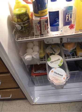 a reviewer photo of a narrow fridge organizing basket pulled out with yogurts in it