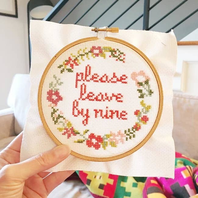 round cross-stitch with the words 'please leave by nine' embroidered in the middle with flowers embroidered around the edge