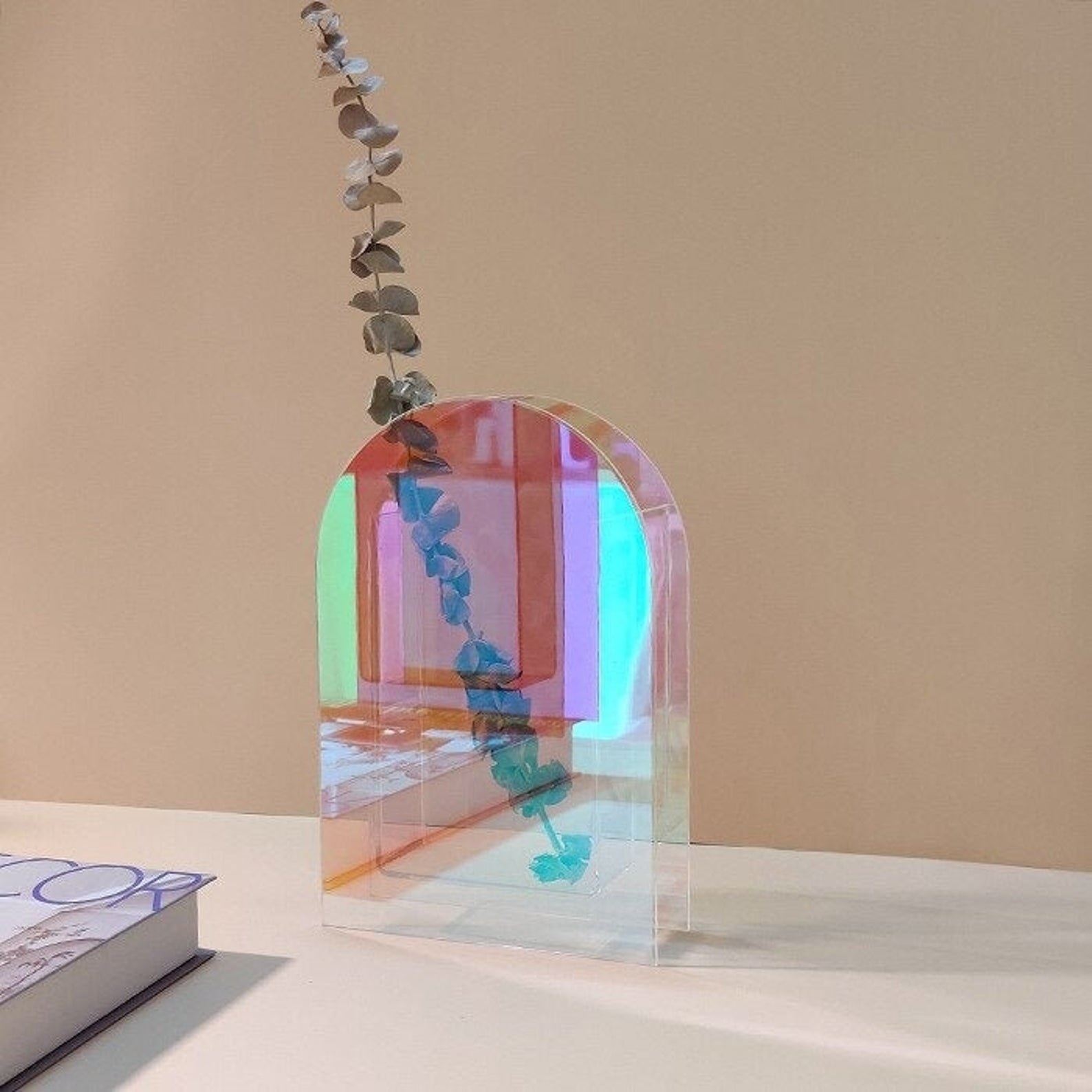 arc-shaped iridescent vase with green plant strand on desk 