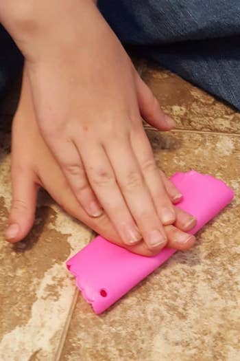 a pair of hands using the pink silicone tube to peel garlic 