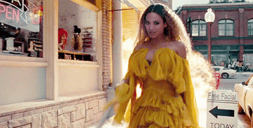 GIF of Beyonce swinging in a bat and wearing a yellow dress with an explosion behind her in the &quot;Hold Up&quot; video