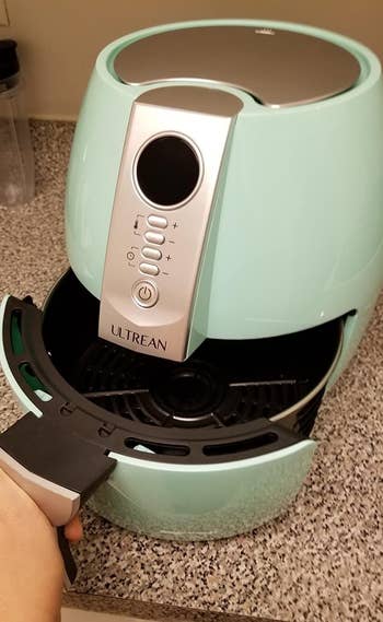 a reviewer photo of a mint green air fryer with a hand pulling open the drawer 