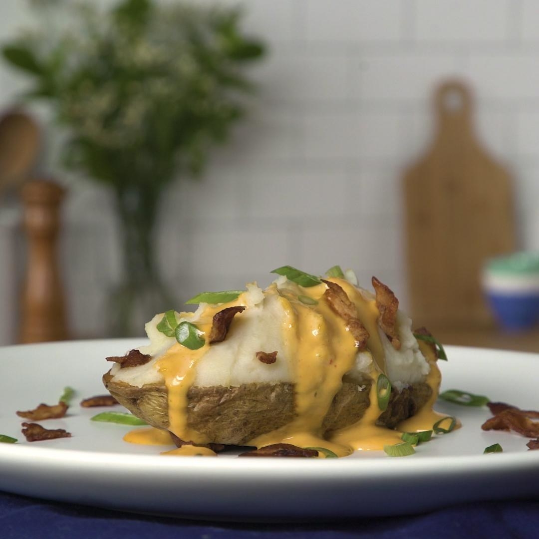 A baked potato loaded with queso, bacon, and chives.