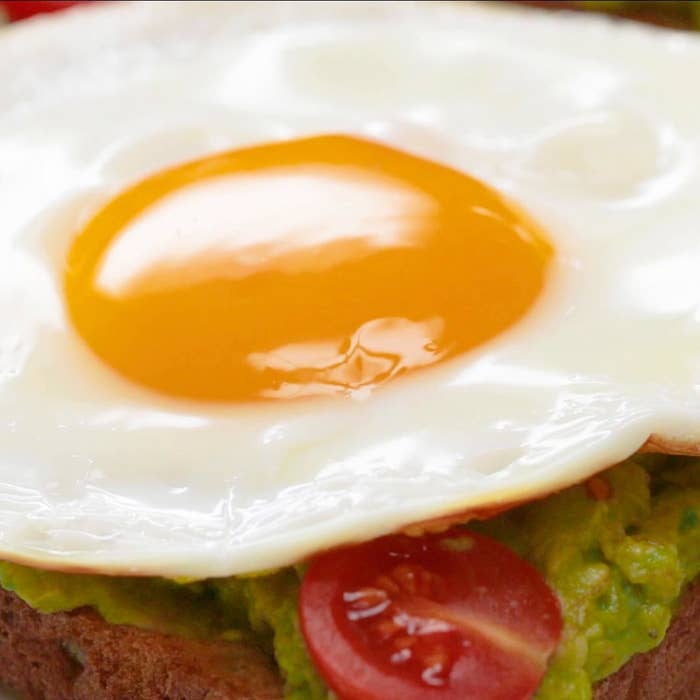 Avocado toast with tomatoes and a fried egg with runny yolk