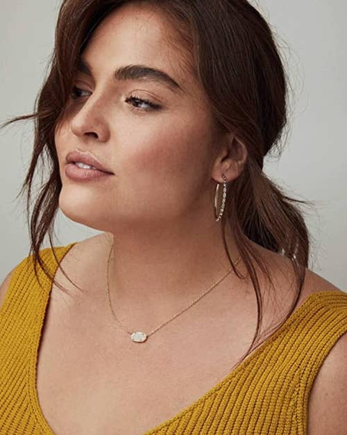 a model wearing a gold chain necklace with a white stone pendant 