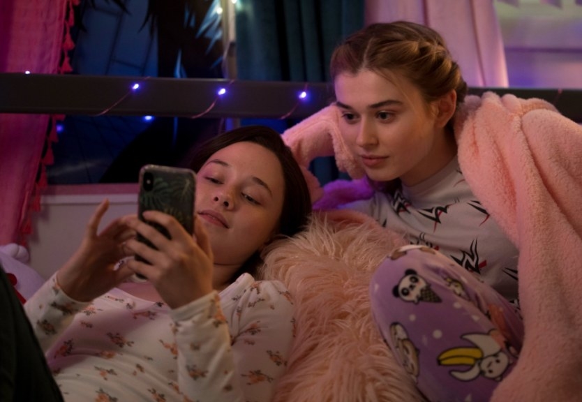 Erin looks at her phone with her friend beside her