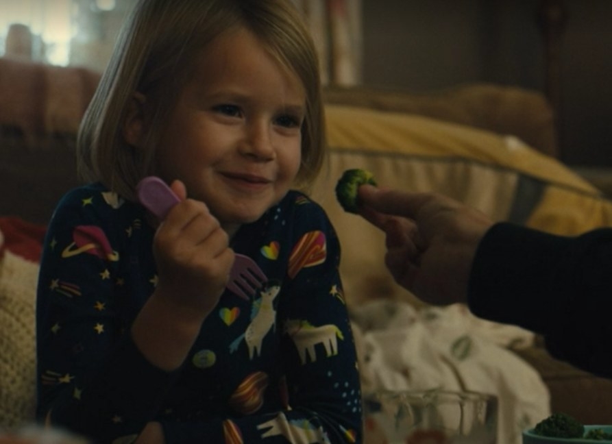 Katie&#x27;s daughter smiles as her grandmother holds a piece of broccoli in front of her face