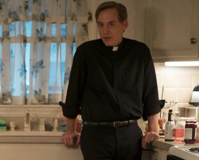 Father Hastings leans on the kitchen counter