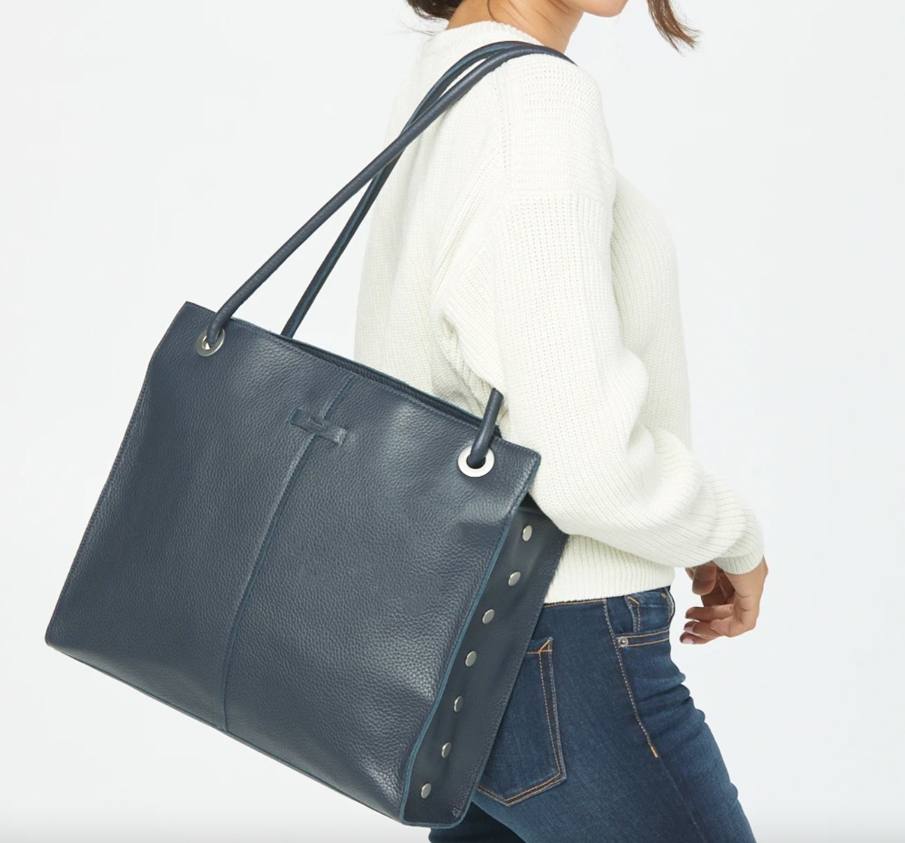 The leather tote bag in french navy being worn by a model in a white sweater
