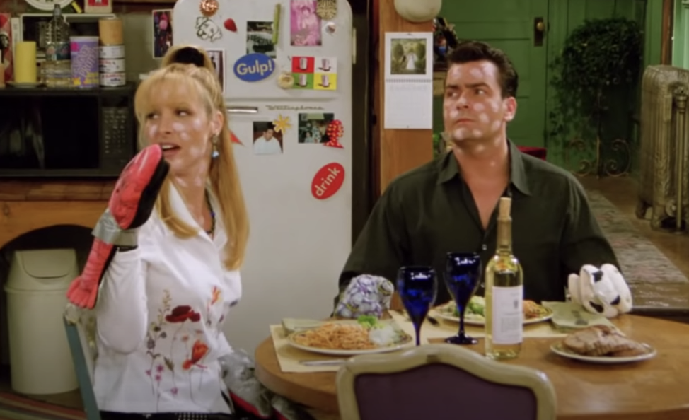 Phoebe and Ryan sit at a dinner table with calamine lotion on their faces and oven mitts duck-taped to their hands