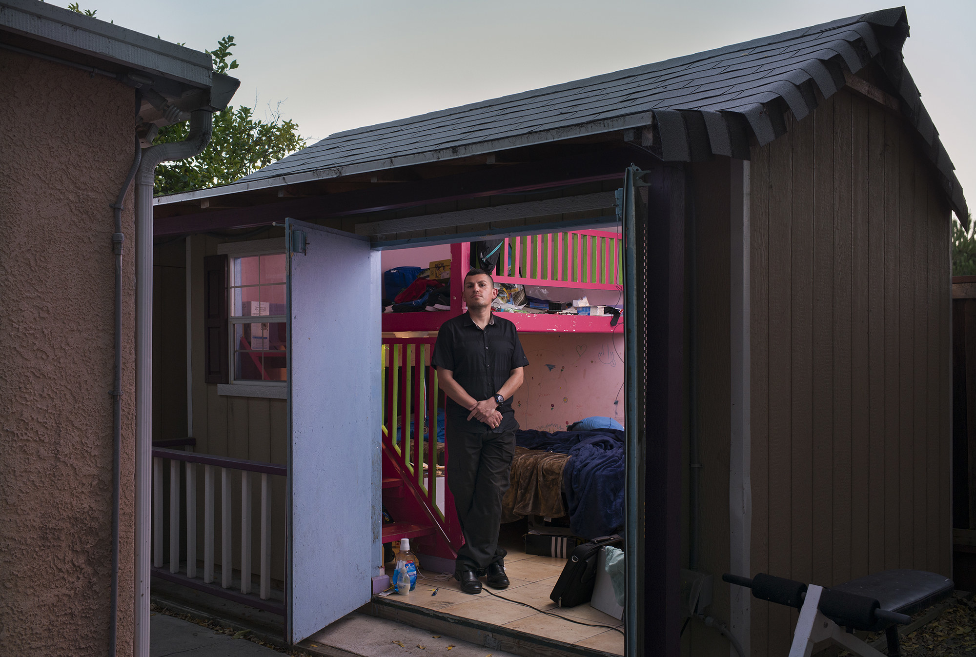 A man stands in the doorway of a small home where he lives