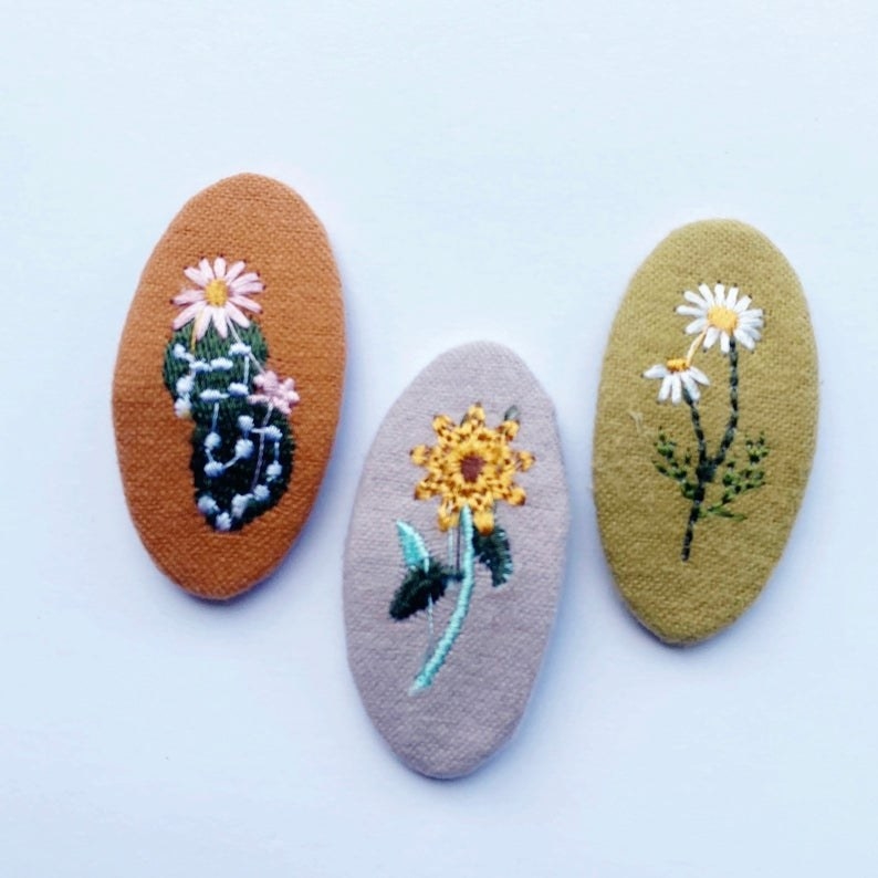 brown, gray, and olive oval-shaped clips each with a different embroidered flower