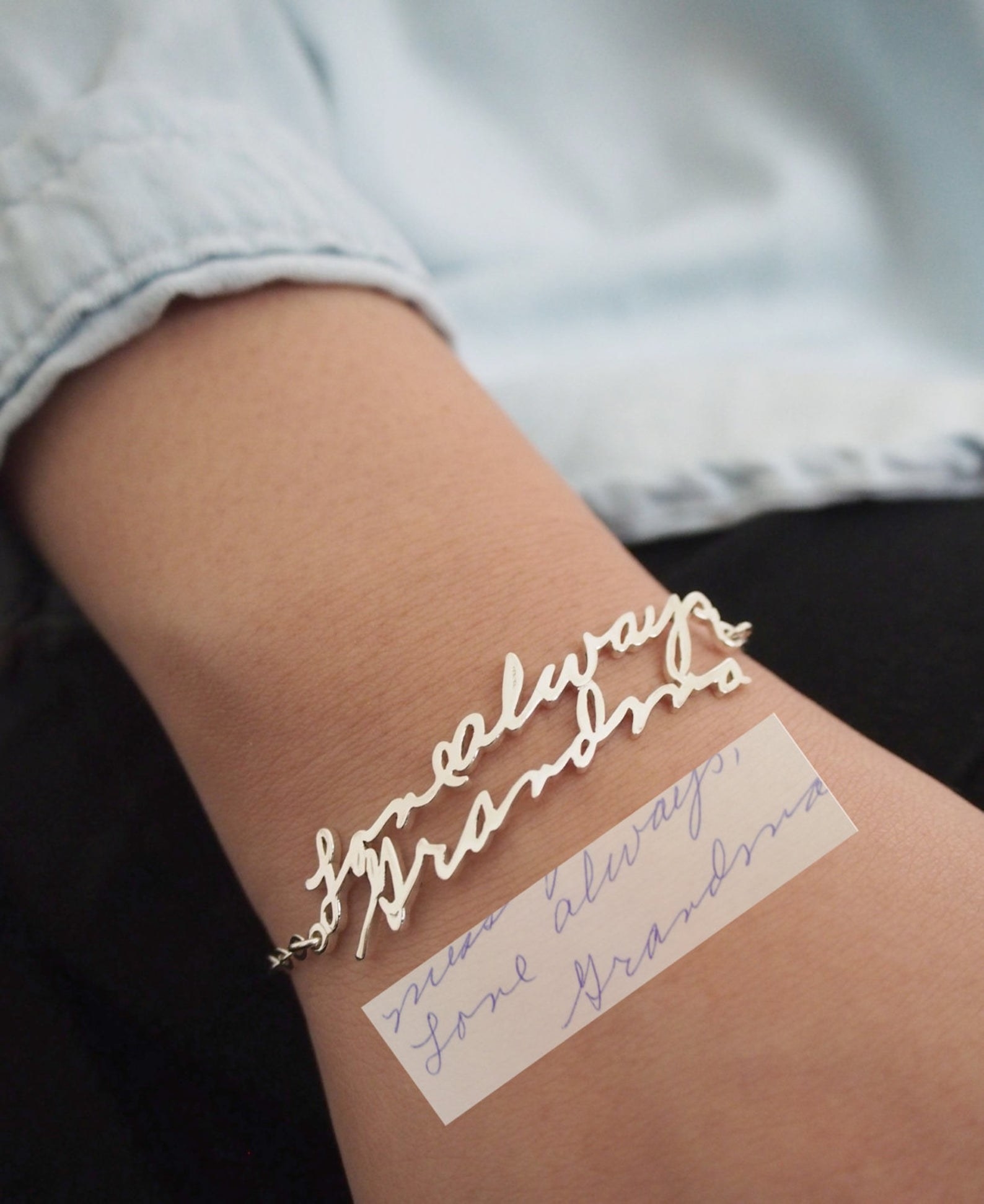 close-up of a model wearing a bracelet featuring golden words from a note form their grandma. The bracelet says &quot;Love always, Grandma&quot; just like the handwritten note also in the image